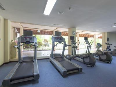 Helles Fitnessstudio mit Laufbändern und Fahrrädern vor großen Fenstern.