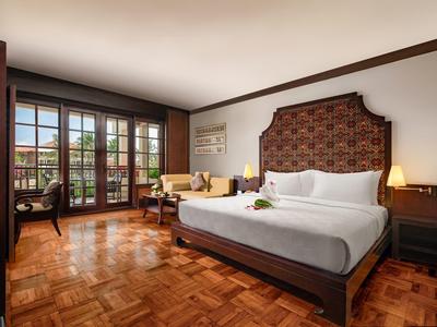 Elegant hotel room with large bed, wooden floor, and floor-to-ceiling windows overlooking terrace.