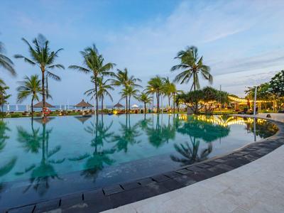 Pool with palm trees and lounge area on the beach at sunset.