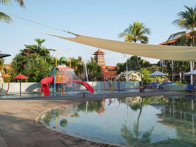 Children's splash pool with slide and water pool in a tropical hotel setting under sunlight