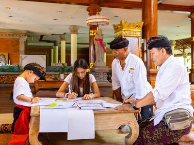 Vier Personen in traditioneller Kleidung arbeiten an einem Tisch in einem offenen Raum mit Holzsäulen.