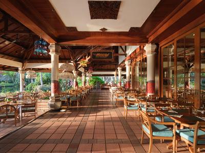 Offener Restaurantbereich mit Holztischen und Stühlen in einer tropischen Umgebung.