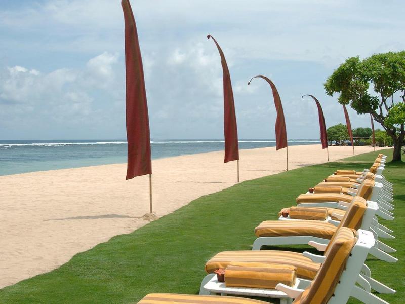 Rows of lounge chairs with yellow cushions on the beach under waving flags.