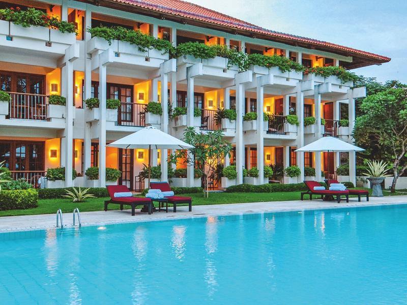 Modern hotel with pool, lounge chairs, and white umbrellas in a tropical setting