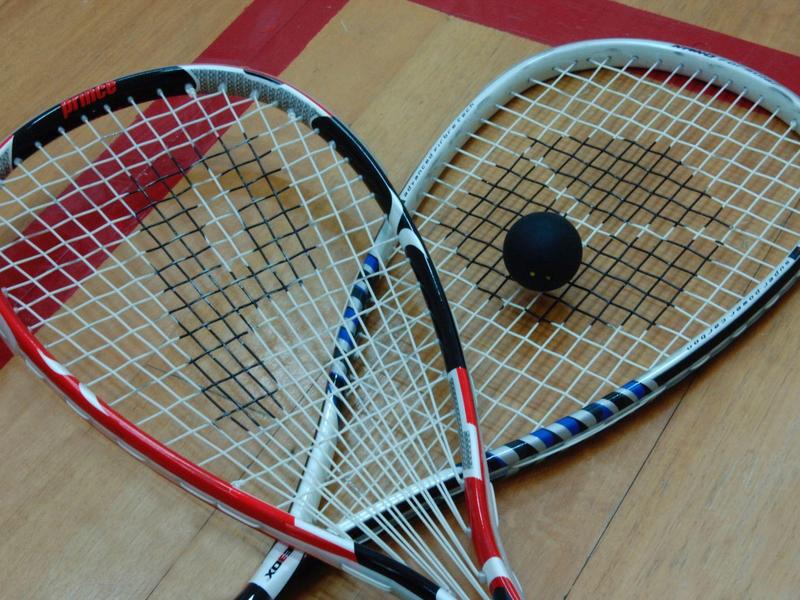 Two squash rackets and a squash ball on a wooden floor with red lines.