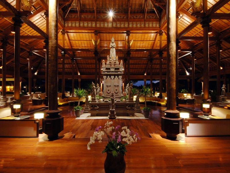 Elegant hotel lobby with wooden interior and central flower arrangement under warm lighting.