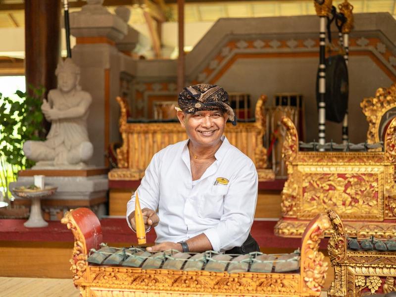 A man in traditional clothing sits in front of an ornately decorated instrument in a temple.