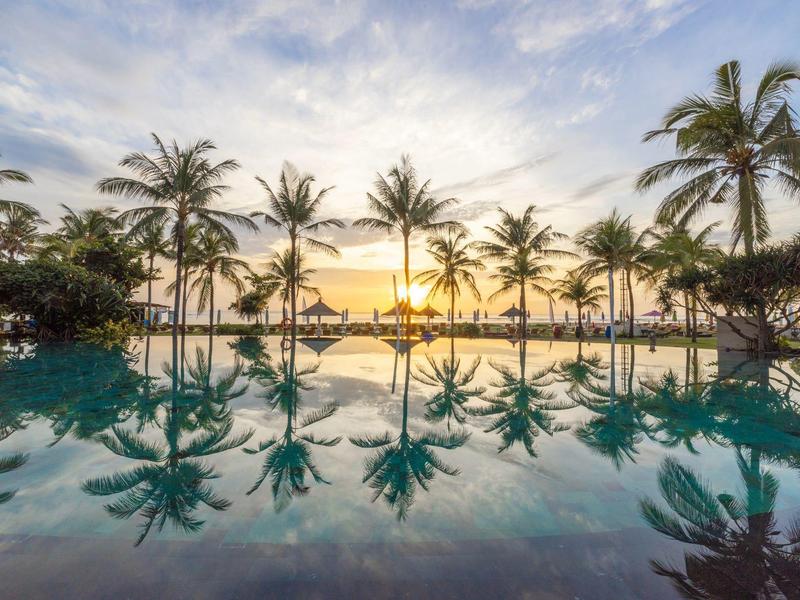 Sunset over a pool with palm trees and reflective water.