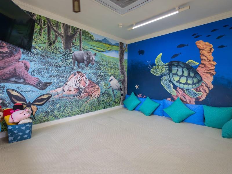 Kids' corner with colorful cushions and wall murals of sea turtles and forest animals.
