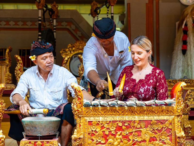 Two musicians in traditional attire play a gold-decorated gamelan instrument.