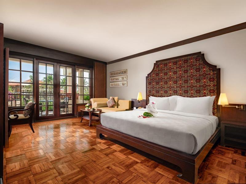 Elegant hotel room with large bed, wooden floor, and floor-to-ceiling windows overlooking terrace.