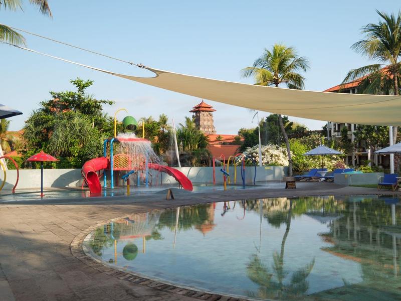 Children's splash pool with slide and water pool in a tropical hotel setting under sunlight