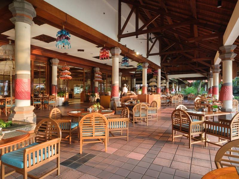 Open hotel restaurant area with many wooden chairs, tables, and traditional decorations.