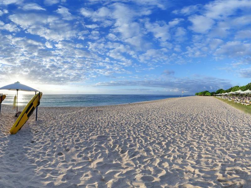 Wide sandy beach with umbrella and chairs under cloudy sky by the sea.