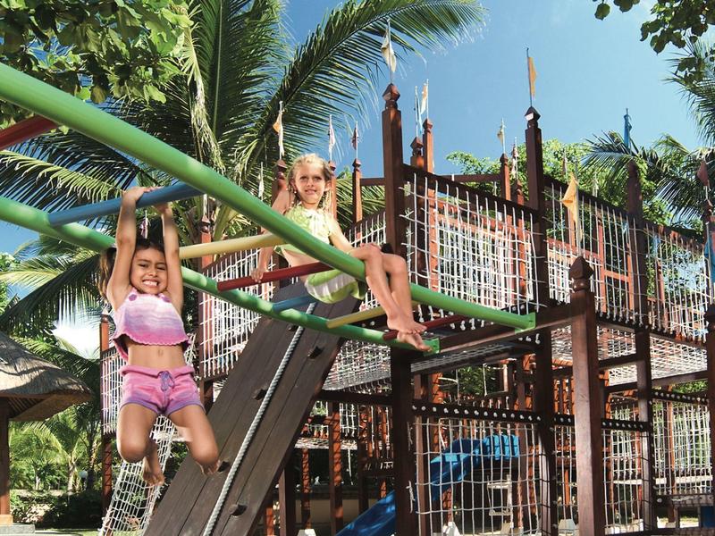 Two children playing on a playground with palm trees and blue sky in the background.