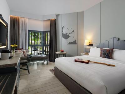 Modernes Hotelzimmer mit großem Bett, Schreibtisch, Sessel und Balkon mit Blick ins Grüne.