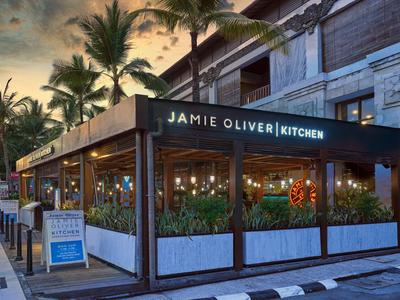 Außenbereich eines Jamie Oliver Restaurants bei Sonnenuntergang mit Palmen im Hintergrund.