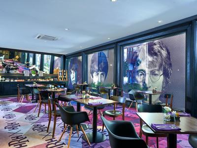 Modern eingerichteter Hotelrestaurantbereich mit buntem Teppich und großflächiger Kunst an den Wänden.