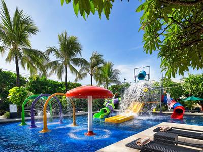 Bunter Wasserpark mit Fontänen, Rutschen und Liegestühlen unter Palmen bei sonnigem Wetter.