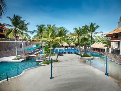 Blick auf einen Poolbereich mit Palmen und Liegestühlen unter blauem Himmel in einem Resort.