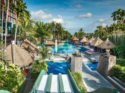 Großer Poolbereich in einem tropischen Resort mit Palmen und Sonnenschirmen.