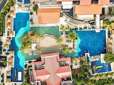 Luftaufnahme eines Hotels mit mehreren Pools, Sonnenschirmen und Grünflächen.