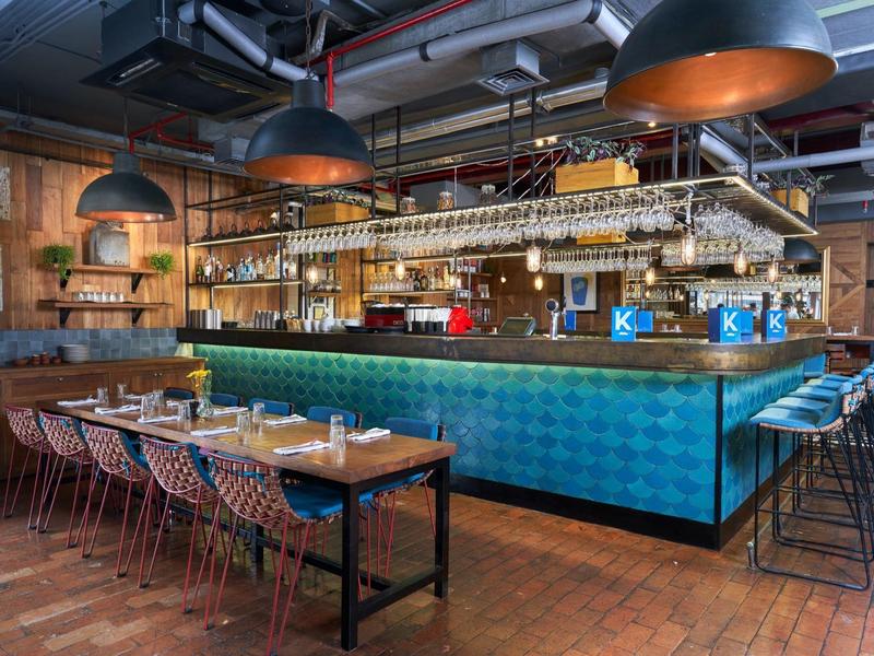 Interno moderno di bar dell'hotel con bancone blu, sgabelli e tavoli in legno con sedie.