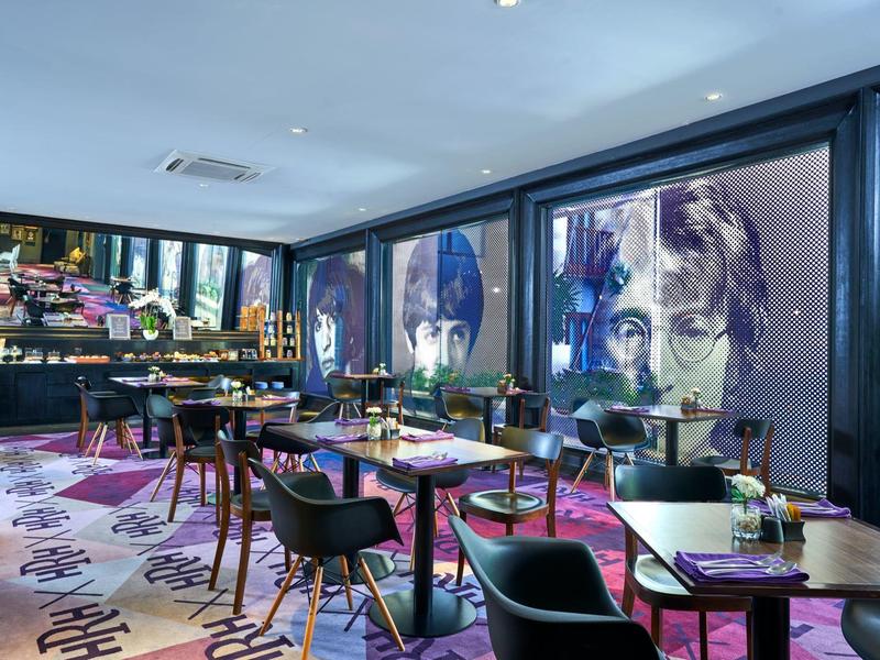 Area pranzo d'hotel moderna con tappeto colorato e grandi opere d'arte alle pareti.