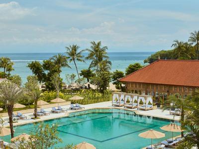 Hotelpool mit Liegestühlen, Palmen und Blick auf das Meer bei klarem Himmel.