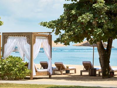 Strandhotel mit Lounge-Bereich, Schaukeln und Blick aufs Meer unter blauem Himmel.