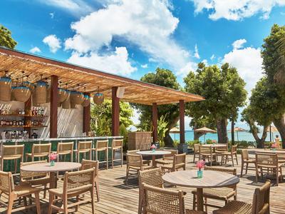 Freiluftrestaurant mit Holzmöbeln und Blick auf das Meer unter blauem Himmel.