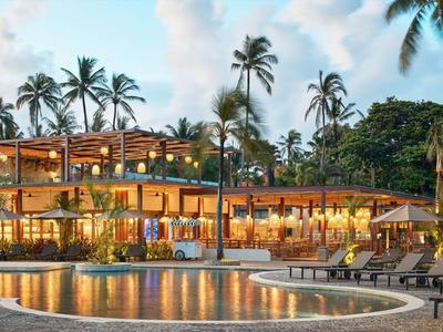 Modernes Resort mit beleuchteten Pool und Liegestühlen, umgeben von Palmen bei Abenddämmerung.