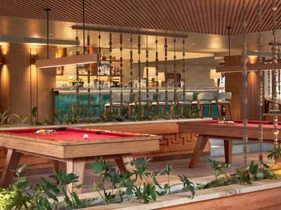 Moderne Hotelbar mit Billardtischen und dekorativen Holzelementen in warmem Licht.