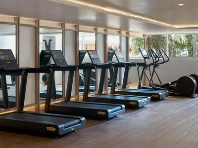Moderner Fitnessraum mit Laufbändern und elliptischen Geräten vor großen Fenstern.