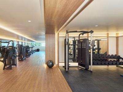 Moderner Fitnessraum mit Holzfußboden, Trainingsgeräten und Hanteln in einem hellen Hotel.