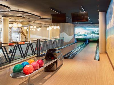 Moderne Bowlingbahn mit bunten Kugeln und digitaler Anzeigetafel in einem Hotel.