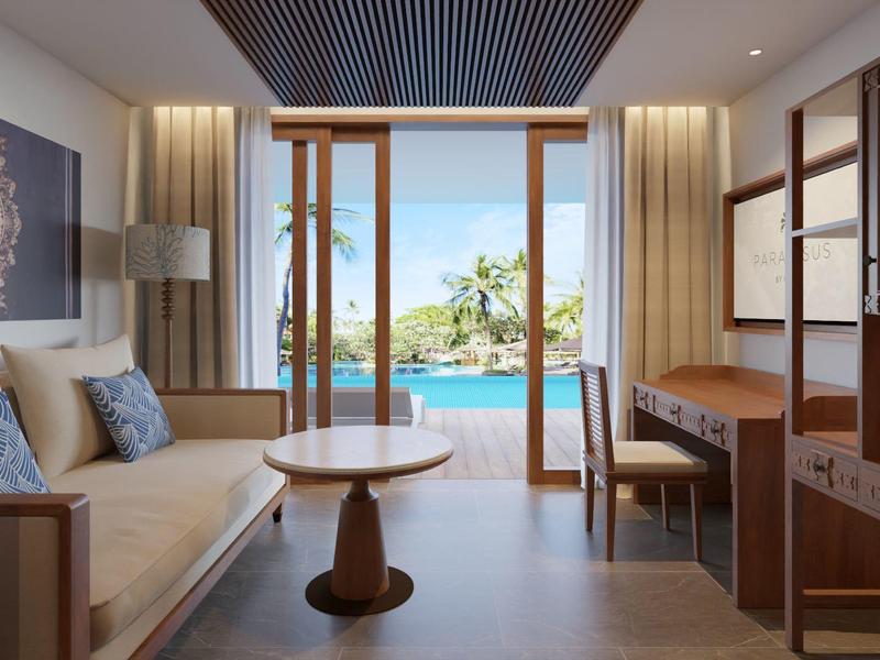 Helles Wohnzimmer mit Holz-Möbeln, Sofa, rundem Tisch und Blick auf tropische Strandlandschaft.