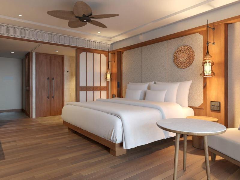 Modernes Schlafzimmer mit großem Bett, Holzboden, Deckenventilator und gemütlichem Sitzbereich.