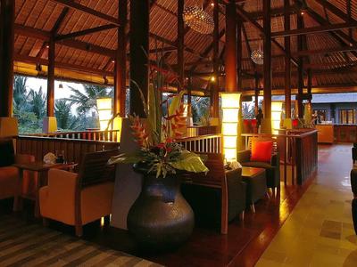 Gemütliche Hotel-Lounge mit Holzdach, Pflanzen und bequemen Sesseln bei Abendlicht.