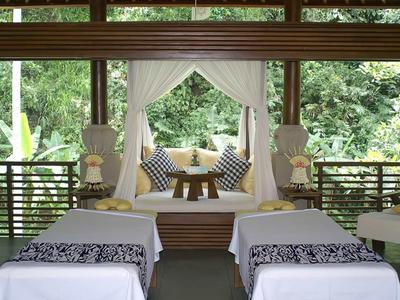 Zwei Massageliegen mit weißen Decken und schwarzem Muster, dahinter dekorative Ruheecke mit Kissen.