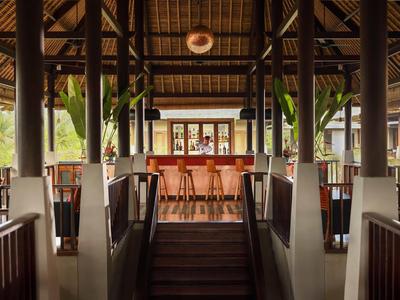 Offene, moderne Bar mit Holzdecke, Stufen, hohen Stühlen und Pflanzen im hellen Ambiente.