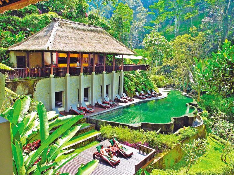 Ein tropisches Resort mit Strohdach, grünem Pool und Liegestühlen, umgeben von dichter Vegetation.