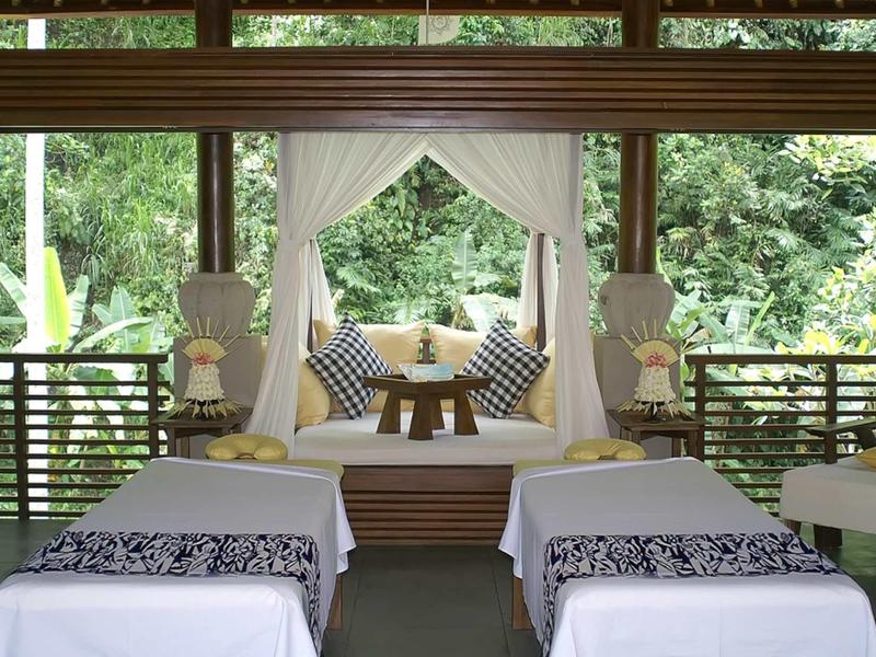 Zwei Massageliegen mit weißen Decken und schwarzem Muster, dahinter dekorative Ruheecke mit Kissen.