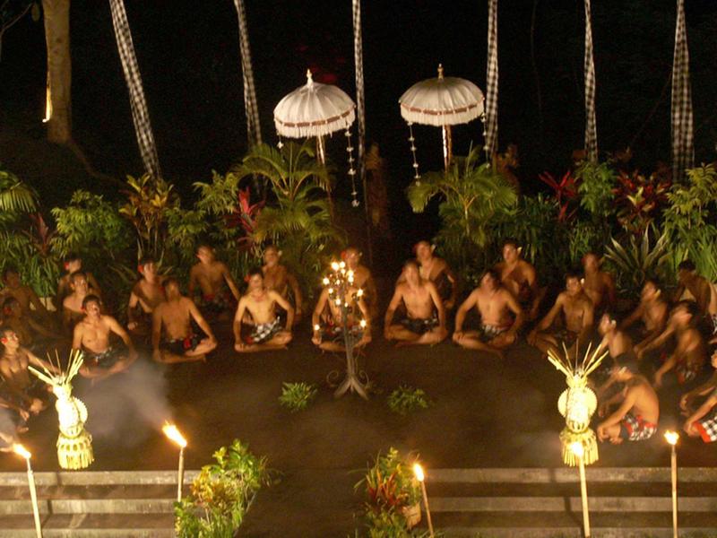 Nächtliche Tanzzeremonie im Kreis mit traditionellem Schmuck, Fackeln und tropischer Pflanzendekoration.