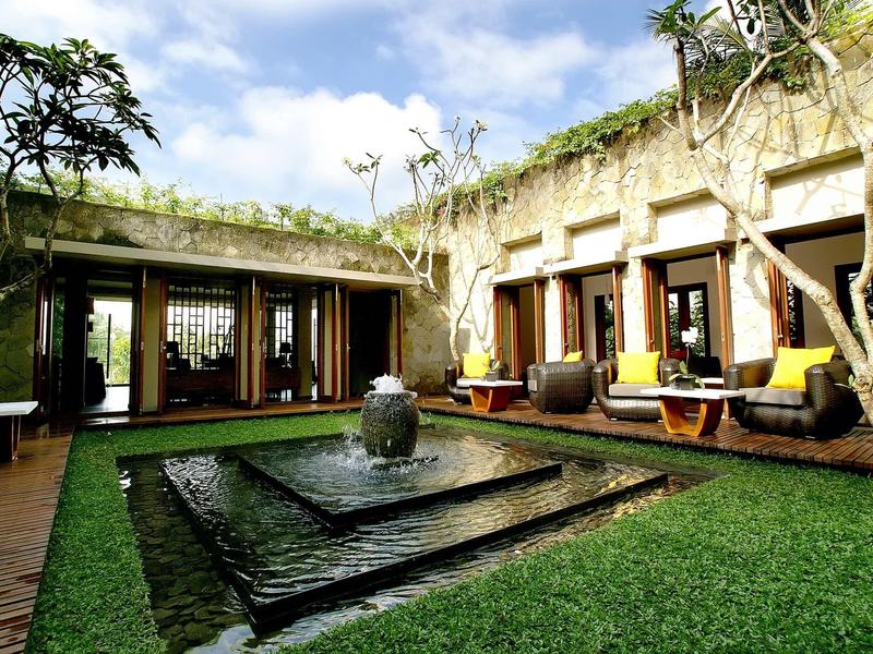 Innenhof mit quadratischem Springbrunnen, grüner Wiese, Holzterrasse und gemütlichen Sitzmöbeln.