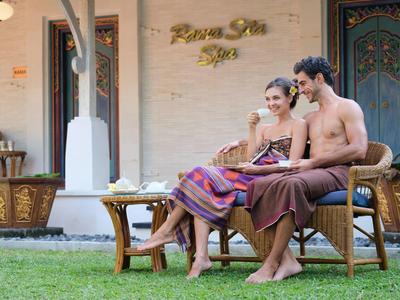 Een stel ontspant op een tuinbank met handdoeken, voor een spa-gebouw.