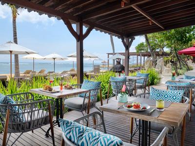 Überdachte Terrasse mit Tischen und Stühlen, Blick aufs Meer und Sonnenschirme.