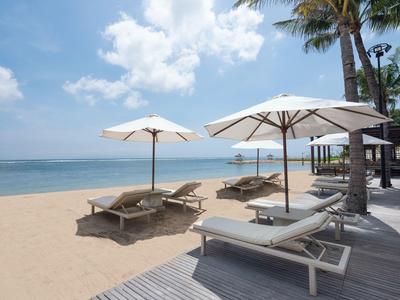 Strand mit Sonnenschirmen und Liegestühlen neben Palmen und einem Steg am Meer.