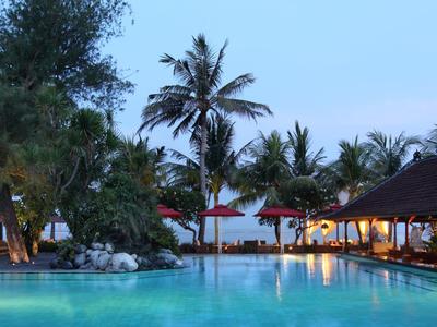 Großer Pool mit Palmen und beleuchteten Holzpavillons bei Sonnenuntergang am Strand.