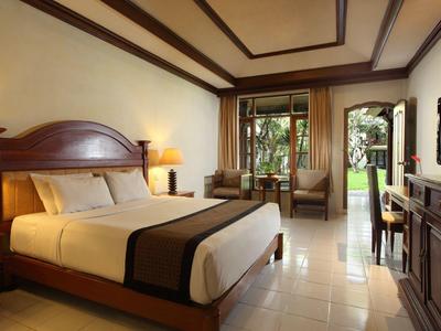 Gezellige hotelkamer met tweepersoonsbed, bank, tv en toegang tot terras met uitzicht op tuin.